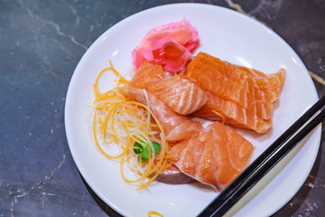 Selective Focused Japanese salmon sashimi (fresh fatty salmon meat) decorated with grated turnip and carrot in white dish on marble table background. Nutrition, Traditional Oriental Asian Food concept
