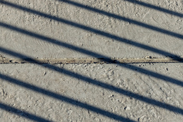 Diagonal shadow lines on concrete surface with horizontal line of separation of concrete slabs in the center.