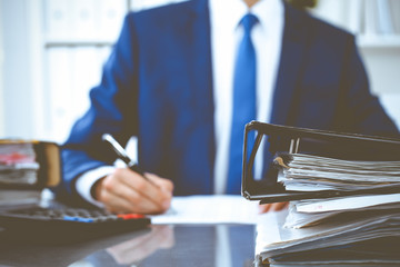 Binders with papers waiting to be processed with businessman or bookkeeper back in blur. Accounting...
