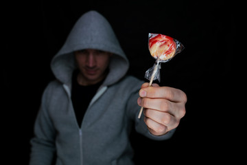 Angry man in a hood holds a lollipop in his hand and holding out to his victim, for luring....