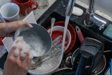 Female hands wash a gray bowl over the sink in the kitchen with a dishwashing detergent. Household chores. Side view