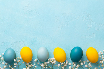 Colorful Easter eggs with flowers on blue background. Top view. Copy space.