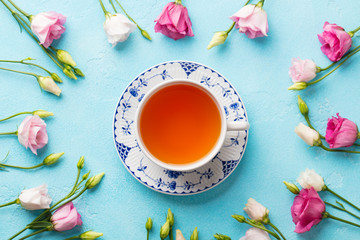 Cup of tea with pink flowers eustoma on blue background. Flat lay composition. Top view.