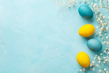 Colorful Easter eggs with flowers on blue background. Top view. Copy space.