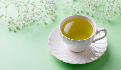 Green tea in a white cup with gypsophila flowers on green pastel background. Close up.