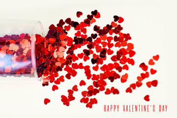 The glass lies on a light background. Red hearts poured out of it. The concept for Valentine's Day