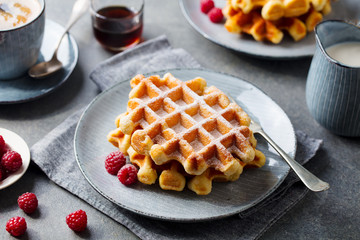 Breakfast Belgian waffles with maple syrup and fresh raspberry. Grey background.
