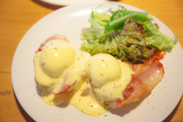 Selective Focused Eggs Benedict, a sandwich consists of 2 halves of English muffin topped with poached egg, bacon or ham and hollandaise sauce. American breakfast or brunch dish. Morning meal concept