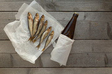Smoked herring fish with a bottle of beer on a wooden background.