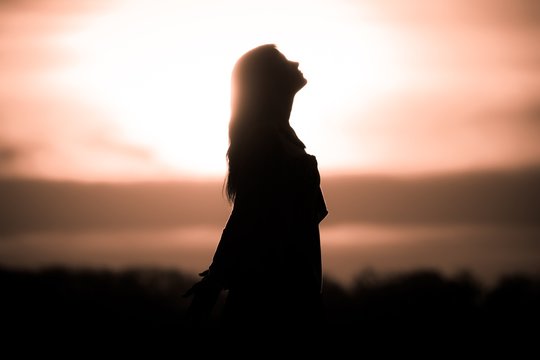 Youth woman soul at golden sun meditation awaiting future times. Silhouette in front of sunset or sunrise in summer nature. Symbol for healing burnout therapy, wellness relaxation or resurrection