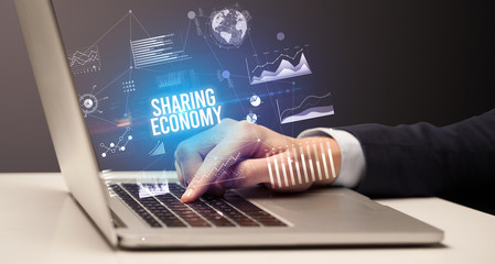 Businessman working on laptop with SHARING ECONOMY inscription, new business concept