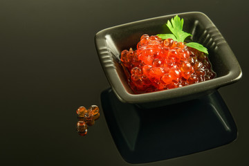 Red fresh caviar on the black  platter and on the black reflective background.
