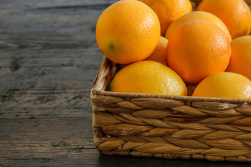 Fresh oranges in the basket on the wooden natural background closeup.