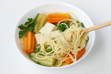 Traditional asian soup with tofu cheese, noodles, carrots and zucchini on white background, dish usually contains bouillon and vegetables, Horizontal orientation