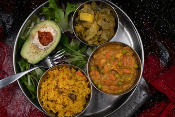 Indian food platter with serving bowls: mixed veggetable curry, cabbage curry, rice pilaf, salad and avocado