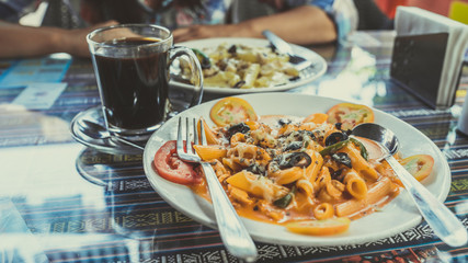Delicious pasta with tomato sauce. Silverware placed on plate of palatable pasta with tomato sauce and olives on ornamental table in cafeteria
