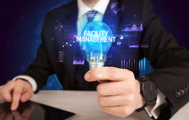 Businessman holding lightbulb with FACILITY MANAGEMENT inscription, Business idea concept