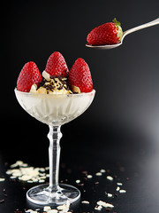 Strawberries with cream in glass cup on black background.