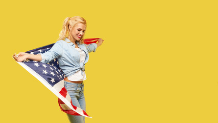 American girl. Happy young woman in denim clothes holding USA flag on yellow background. Banner. Copy space for text. football fan