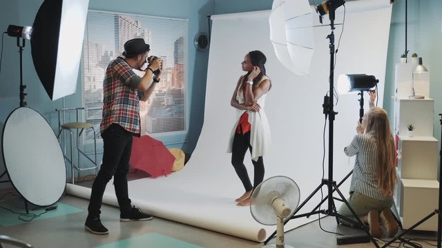 Backstage of the photo shoot: assistant adjusting the spotlight while photographer taking photos of pretty black model