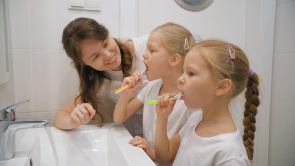 Obraz na płótnie Canvas Mother and daughters brushing teeth together
