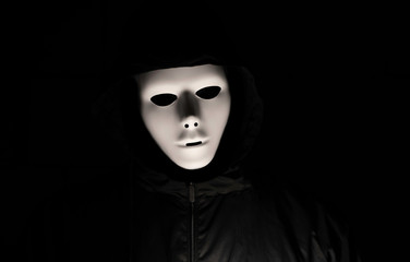 Scary white mask in the dark. Spooky guy in black jacket and white masquerade. Black, invisible...