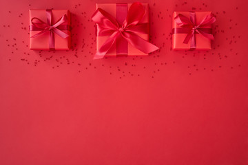 Red gift boxes and ribbon bows on red background. Flat lay,  top view with copy space. Christmas, party or valentine day concept.