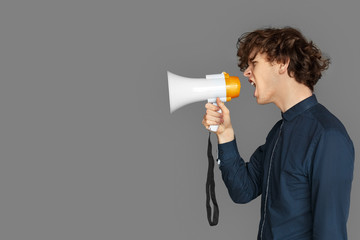 Copy Space for Text or Product. Teenager boy standing isolated on grey shouting emotional at megaphone