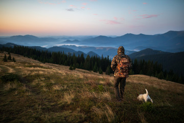 Hunter man dressed in camouflage in the mountains at sunrise. Hunter with dog in the mountains - 314571755