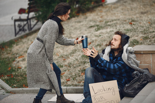 Homeless In A City. Man Asking For Food. Man With A Tablet. Girl Helping A Homeless