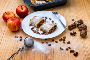 Apple roll pie - Apple Strudel. Pie with apples, cinnamon, walnuts and raisins, sprinkled with powdered sugar in a plate on a wooden table 