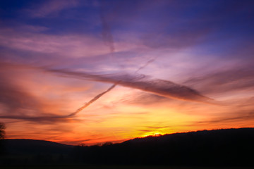 Beautiful multicolored sunset. Cumulonimbus and very colorful stratus in a dramatic sky. Sun disappearing behind a hill.