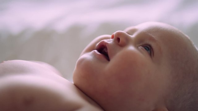 6 Month old baby looks up and smiles wide while laying on bed slow motion r3d