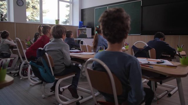 Diverse elementary school students attentively listening to mixed race female teacher using geographic globe during class. Curious schoolchildren studying geography at lesson in primary school