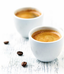 Two cups of coffee on bright wooden background.