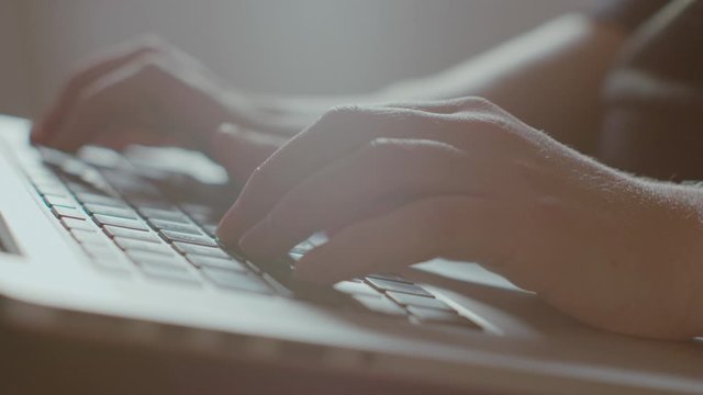 Close up of young female hands typing away writes on a laptop computer keyboard in slowmotion and backlit from a window. Lens flares. UHD.