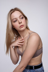 Obraz premium beauty portrait of sexy caucasian woman with long blond hair posing in beige lingerie and blue jeans on white studio background. model tests of pretty girl in bra. attractive female with clean skin
