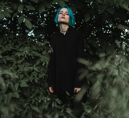 Beautiful young girl with blue hair in a black dress on a background of greenery
