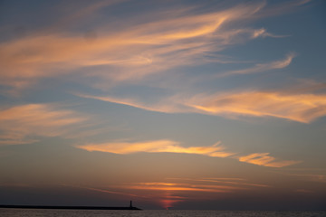 Silhouette of a lighthouse on the horizon in the rays of the setting sun. Colorfull sky