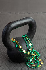 Black iron kettlebell with green and gold beads on a black gym floor, holiday fitness