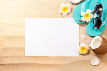 Summer Holidays. Blue slippers, sunglasses, coconut and other beach accessories. A blank sheet of white paper for your text on the sand. Top view with copy space.