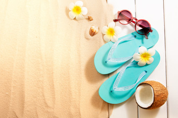 Summer Holidays. Blue slippers, sunglasses, coconut and other beach accessories on sand and white wood background. Top view with copy space.
