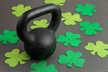 Black iron kettlebell with green shamrocks on a black gym floor, holiday fitness