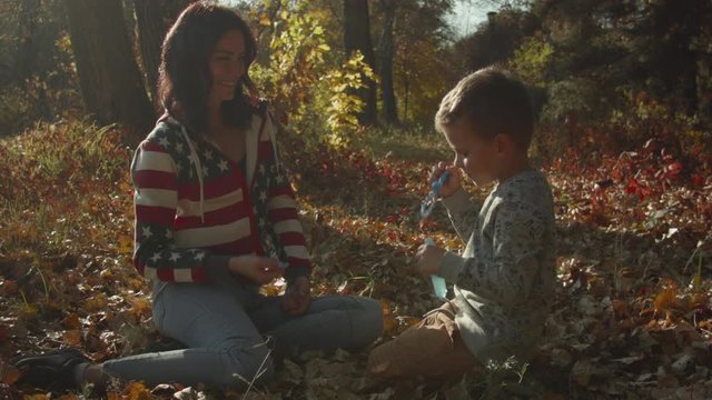 Young Caucasian woman blows soap bubbles with her child in the autumn forest. Recorded in Raw on Blackmagic camera.