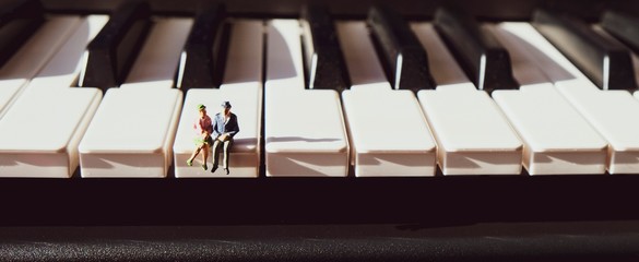 Miniature figurines of an elderly couple, sitting together on the keys of a piano.