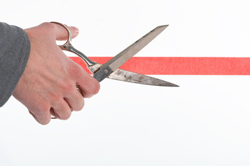 Male hand cutting through red tape with scissors isolated on white with a shallow depth of field...