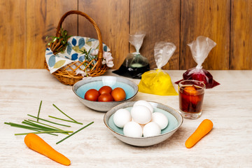 Dying eggs for Easter holiday. White and dyed eggs bowls arranged on vintage oak wood table