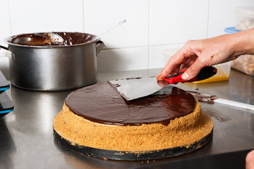 Woman smears chocolate cake with glaze icing, final stage of cooking. Made by hands for confectionery.