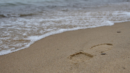 Daytime photo of the surf on a sandy Lake Michigan beach with a footprint in the sand in the foreground