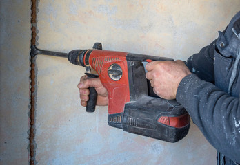 Worker using a jackhammer to drill into wall for electricity installation, on construction site
